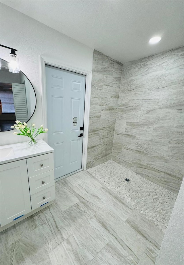 bathroom with tiled shower, vanity, and a textured ceiling