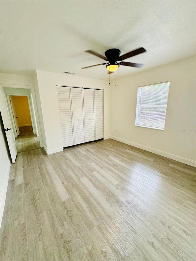 unfurnished bedroom with a textured ceiling, light hardwood / wood-style flooring, ceiling fan, and a closet