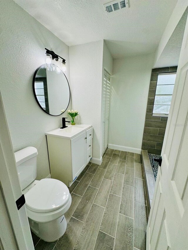 bathroom featuring toilet, vanity, a textured ceiling, and walk in shower