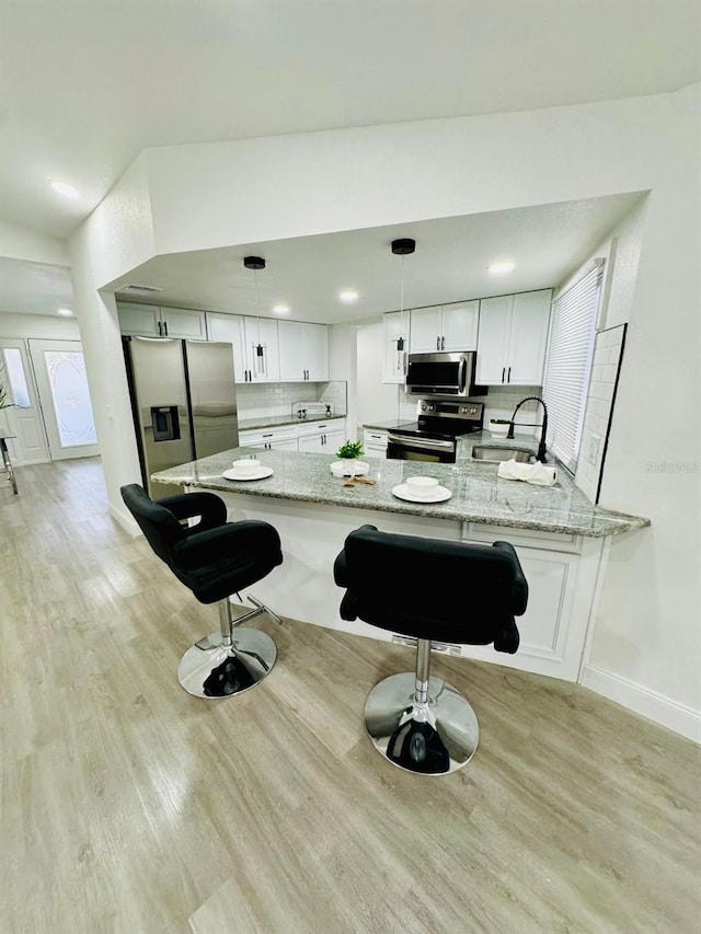 kitchen featuring white cabinets, kitchen peninsula, light stone countertops, pendant lighting, and appliances with stainless steel finishes