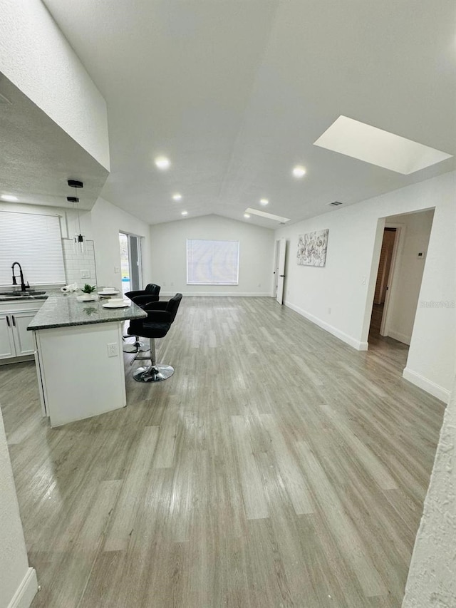 interior space featuring light hardwood / wood-style floors, white cabinetry, a kitchen bar, lofted ceiling, and a center island