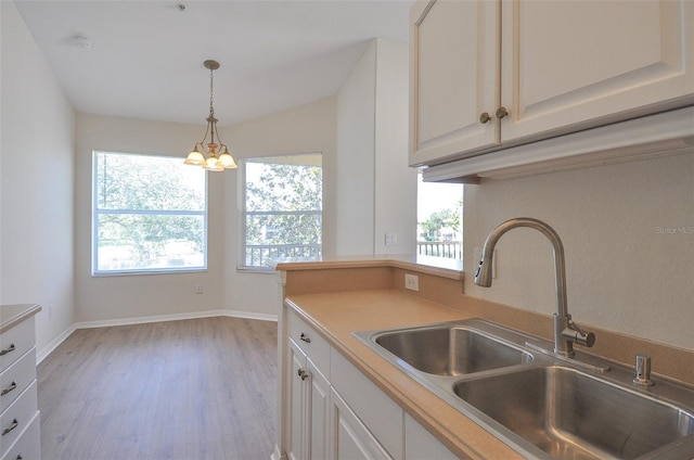 kitchen with sink, white cabinets, light hardwood / wood-style floors, and an inviting chandelier