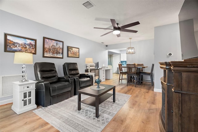 living room with ceiling fan with notable chandelier, a textured ceiling, and light hardwood / wood-style flooring