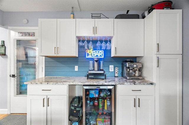 kitchen featuring light hardwood / wood-style floors, light stone counters, backsplash, beverage cooler, and white cabinets