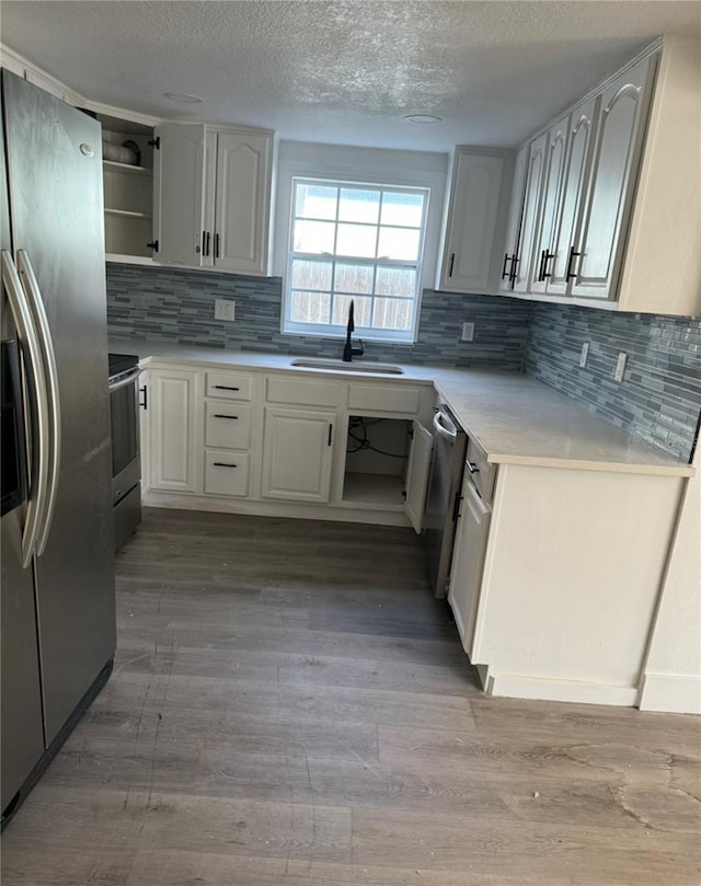 kitchen with light wood-type flooring, appliances with stainless steel finishes, backsplash, sink, and white cabinets