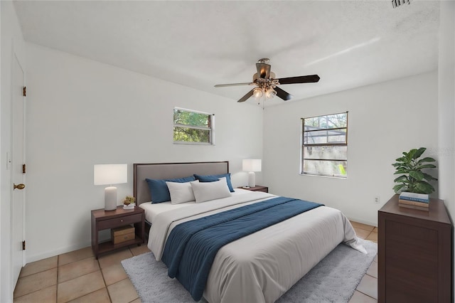 bedroom featuring ceiling fan, multiple windows, and light tile patterned floors