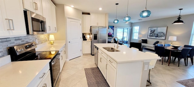 kitchen featuring white cabinetry, an island with sink, appliances with stainless steel finishes, decorative backsplash, and hanging light fixtures