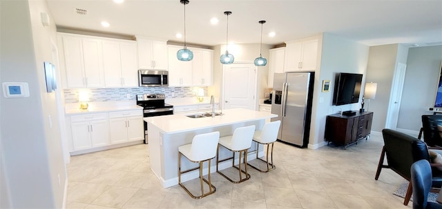 kitchen featuring white cabinetry, an island with sink, appliances with stainless steel finishes, decorative light fixtures, and sink