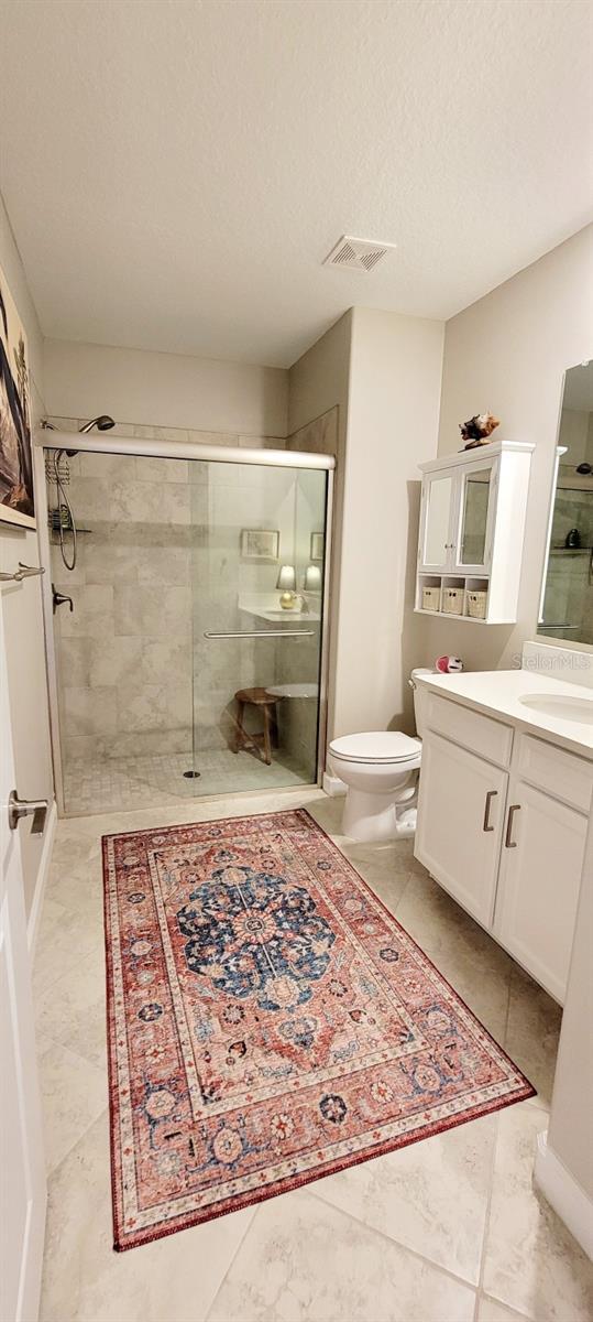 bathroom featuring toilet, a textured ceiling, a shower with door, and vanity