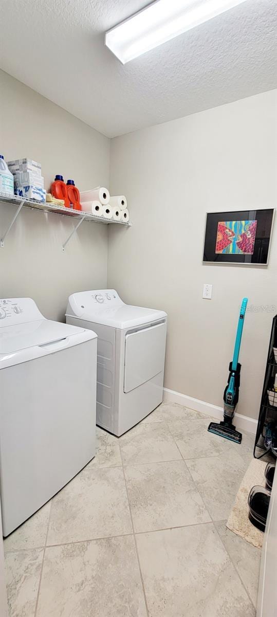 washroom with light tile patterned flooring, washer and dryer, and a textured ceiling