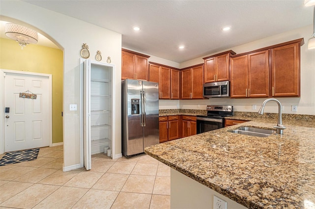 kitchen featuring light tile patterned flooring, stainless steel appliances, stone countertops, sink, and kitchen peninsula