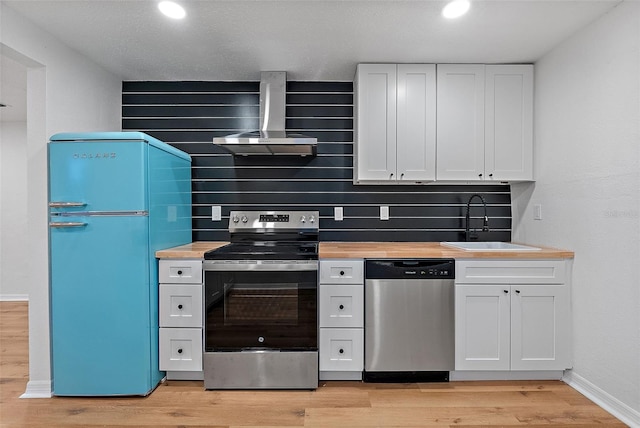 kitchen featuring decorative backsplash, sink, stainless steel appliances, white cabinets, and wall chimney exhaust hood