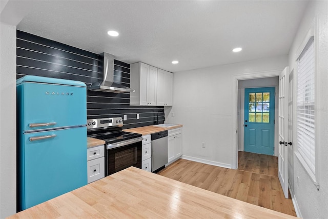 kitchen with white cabinetry, stainless steel appliances, tasteful backsplash, light wood-type flooring, and wall chimney range hood