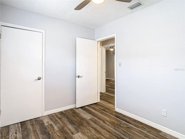 unfurnished bedroom featuring ceiling fan, a textured ceiling, a closet, and dark hardwood / wood-style flooring