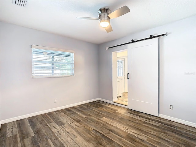 unfurnished bedroom featuring dark hardwood / wood-style flooring, a barn door, and ceiling fan