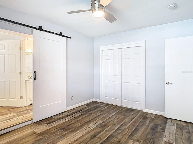 unfurnished bedroom with dark hardwood / wood-style flooring, a closet, a barn door, and ceiling fan