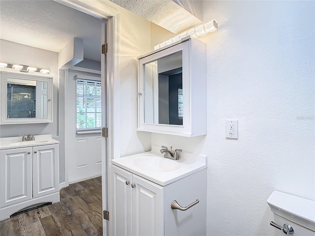 bathroom with wood-type flooring, vanity, toilet, and a textured ceiling