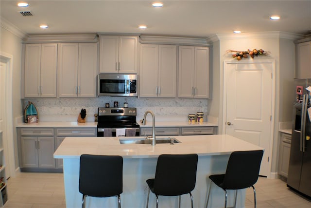 kitchen with sink, tasteful backsplash, gray cabinetry, a kitchen island with sink, and appliances with stainless steel finishes