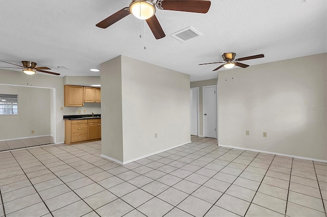 unfurnished living room featuring sink, ceiling fan, a textured ceiling, and light tile patterned flooring