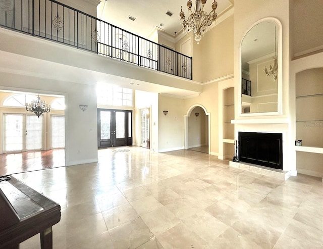 unfurnished living room with a high ceiling, french doors, built in shelves, ornamental molding, and a notable chandelier