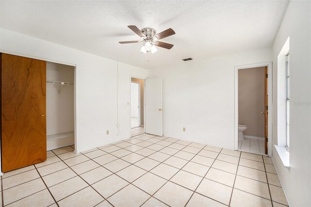 unfurnished bedroom featuring light tile patterned floors, a textured ceiling, ensuite bathroom, ceiling fan, and a closet