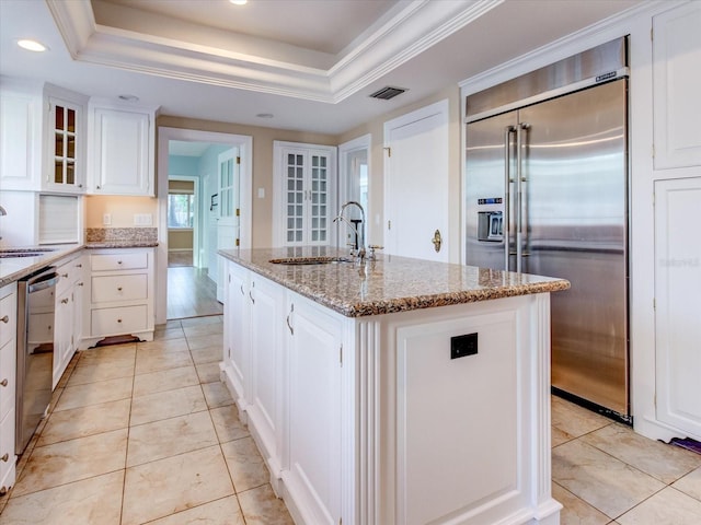 kitchen with a tray ceiling, a kitchen island with sink, white cabinetry, and appliances with stainless steel finishes