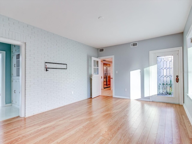 unfurnished room with light hardwood / wood-style floors and brick wall