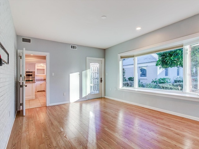 empty room featuring plenty of natural light, brick wall, and light hardwood / wood-style flooring