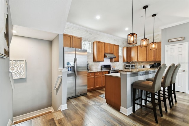 kitchen featuring appliances with stainless steel finishes, ornamental molding, pendant lighting, dark hardwood / wood-style floors, and a breakfast bar area