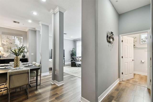 corridor featuring wood-type flooring, ornate columns, and ornamental molding