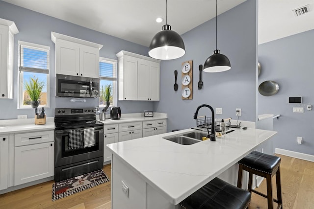 kitchen with white cabinets, sink, a kitchen island with sink, appliances with stainless steel finishes, and decorative light fixtures