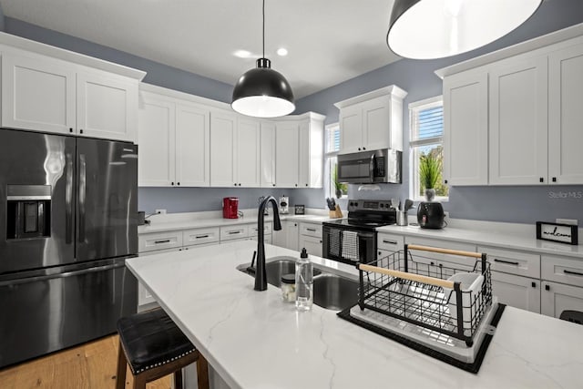 kitchen featuring a kitchen bar, stainless steel appliances, white cabinets, sink, and decorative light fixtures