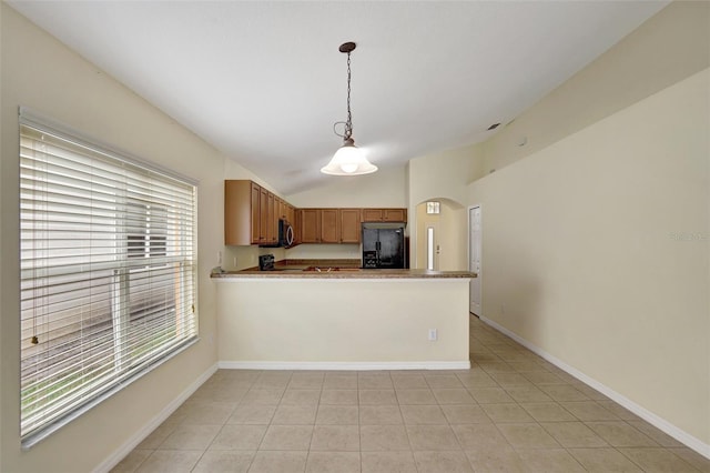 kitchen featuring a peninsula, light countertops, black fridge, stainless steel microwave, and decorative light fixtures