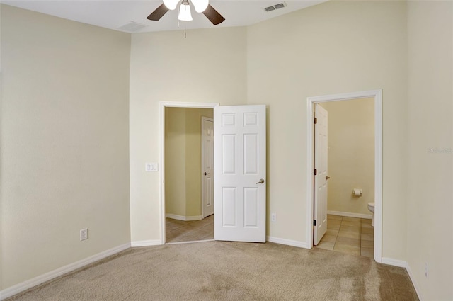 unfurnished bedroom featuring connected bathroom, light carpet, a high ceiling, visible vents, and baseboards