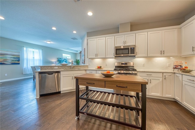 kitchen with light stone counters, appliances with stainless steel finishes, tasteful backsplash, white cabinets, and dark wood-type flooring