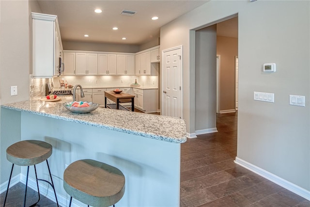 kitchen with kitchen peninsula, tasteful backsplash, stainless steel stove, light stone countertops, and white cabinetry