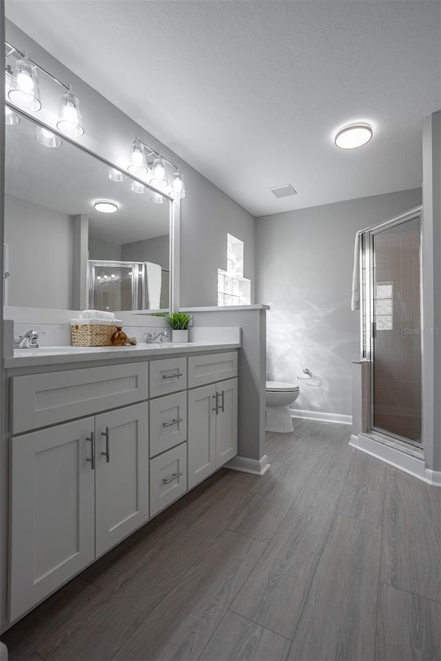 bathroom with vanity, a textured ceiling, hardwood / wood-style floors, toilet, and a shower with shower door