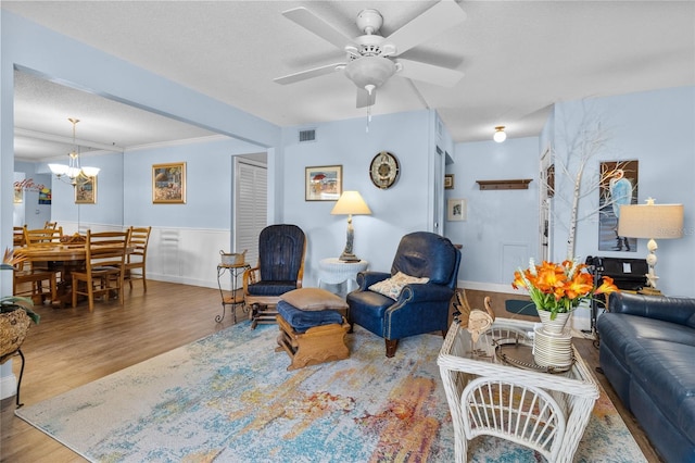 living room featuring a textured ceiling, ceiling fan with notable chandelier, hardwood / wood-style flooring, and crown molding