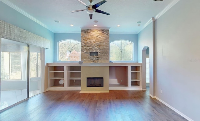 unfurnished living room with wood-type flooring, a fireplace, built in features, ceiling fan, and crown molding