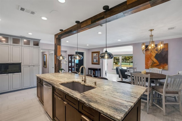 kitchen with pendant lighting, light stone counters, sink, and an island with sink