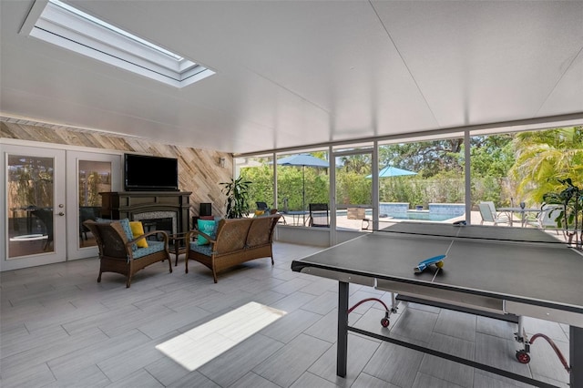 game room featuring french doors, a skylight, plenty of natural light, and wood walls