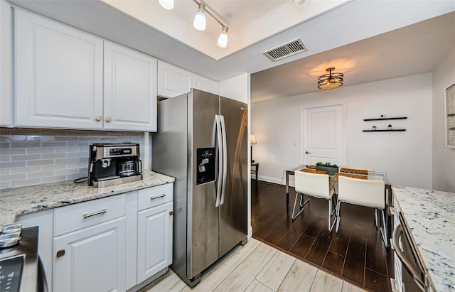 kitchen featuring white cabinets, light hardwood / wood-style flooring, light stone counters, and stainless steel fridge