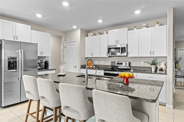 kitchen featuring a kitchen island with sink, white cabinets, light tile patterned floors, and appliances with stainless steel finishes