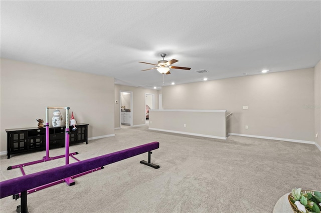 workout area featuring light carpet, ceiling fan, and a textured ceiling