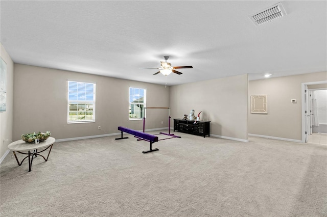 workout room featuring light carpet, ceiling fan, and a textured ceiling