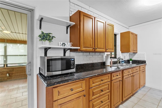 kitchen with decorative backsplash, dark stone counters, sink, and light tile patterned floors