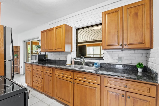 kitchen with light tile patterned flooring, backsplash, appliances with stainless steel finishes, sink, and dark stone countertops