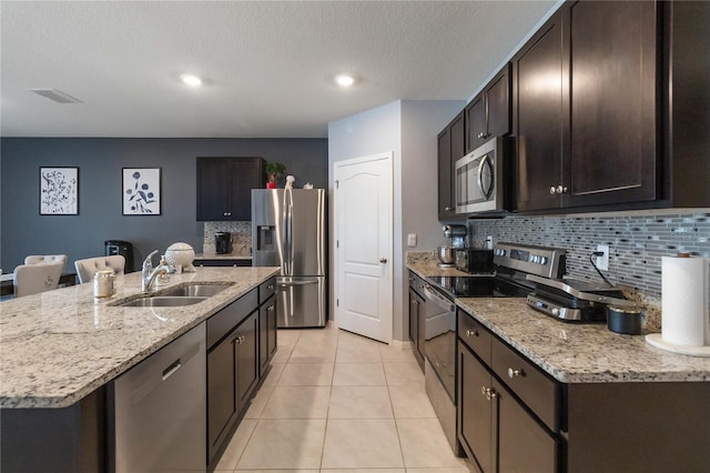 kitchen featuring stainless steel appliances, dark brown cabinetry, light tile patterned floors, sink, and a kitchen island with sink