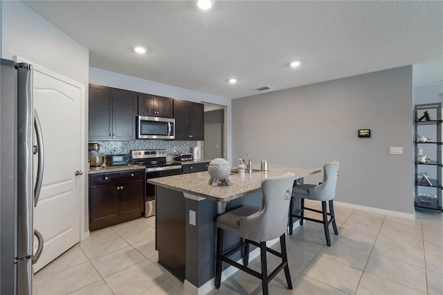 kitchen featuring appliances with stainless steel finishes, dark brown cabinetry, a kitchen breakfast bar, and a kitchen island with sink