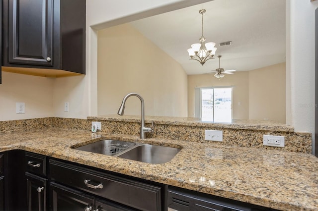 kitchen featuring light stone countertops, pendant lighting, lofted ceiling, ceiling fan with notable chandelier, and sink